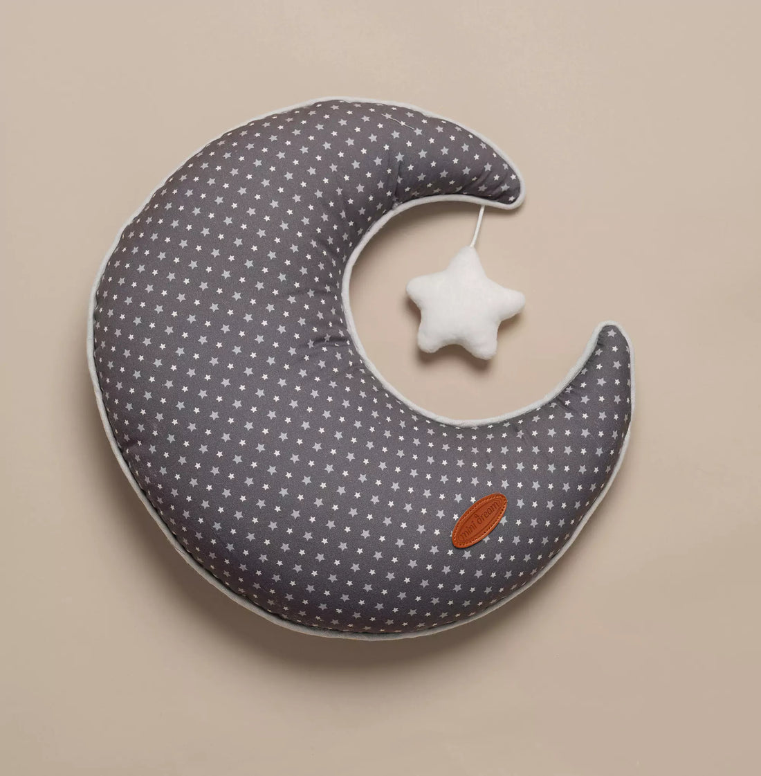 A gray moon-shaped cushion with a star pattern and a white star hanging on it, displayed on a beige background.