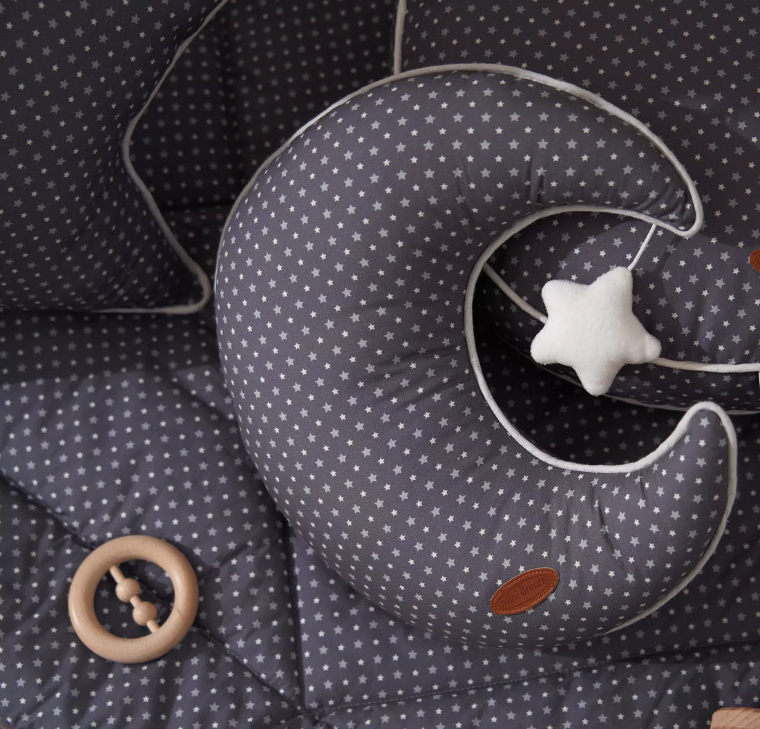 A gray moon-shaped cushion with a star pattern and a white star hanging on it, displayed on a beige background.