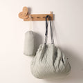 Sage green convertible toy storage bag and its matching small cylindrical travel pouch hanging from a wooden wall peg.