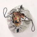 MiniDream sage green playmat partially cinched together into a bag with its black drawstrings, holding an assortment of plush and wooden toys.