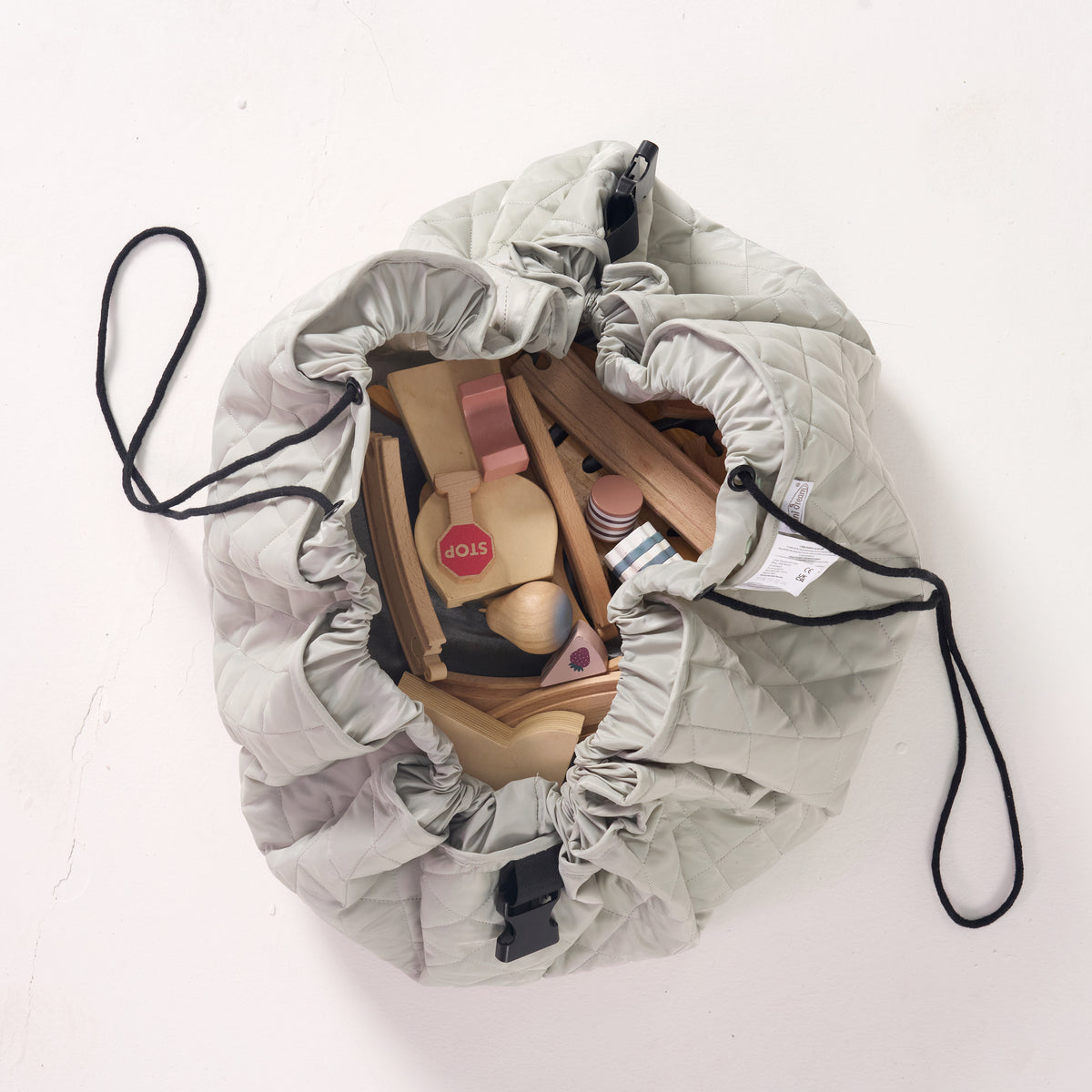 MiniDream sage green playmat partially cinched together into a bag with its black drawstrings, holding an assortment of plush and wooden toys.