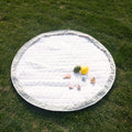 The patterned side of the sage green playmat laid out flat outdoors on green grass, with various baby toys on top.