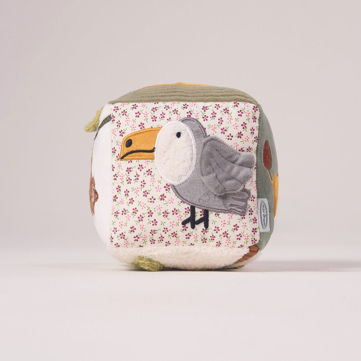 Side view of the MiniDream Jungle Soft Activity Cube displaying a plush toucan bird set against a soft pink and patterned fabric background.