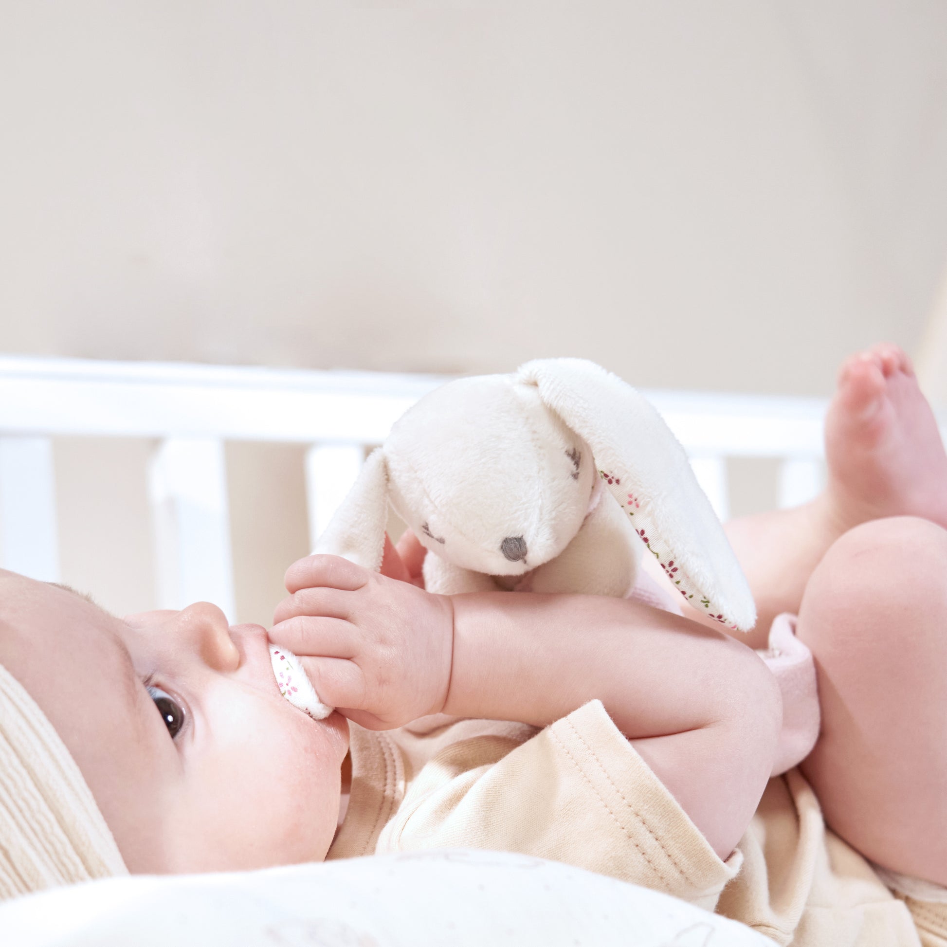 Infant grasping the plush bunny ears of the MiniDream comforter